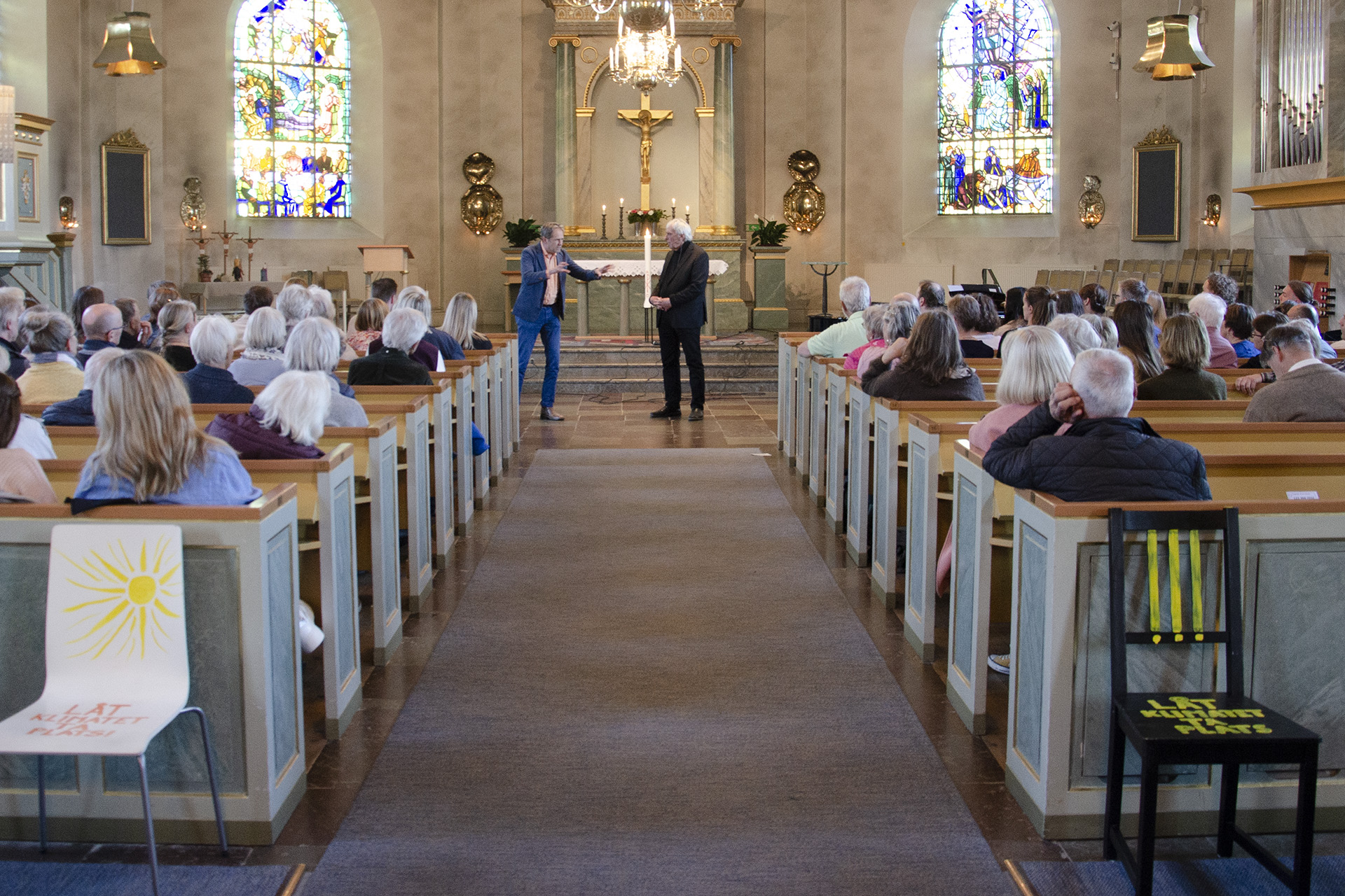 En kyrka med mycket folk i och två män som står längst fram och pratar