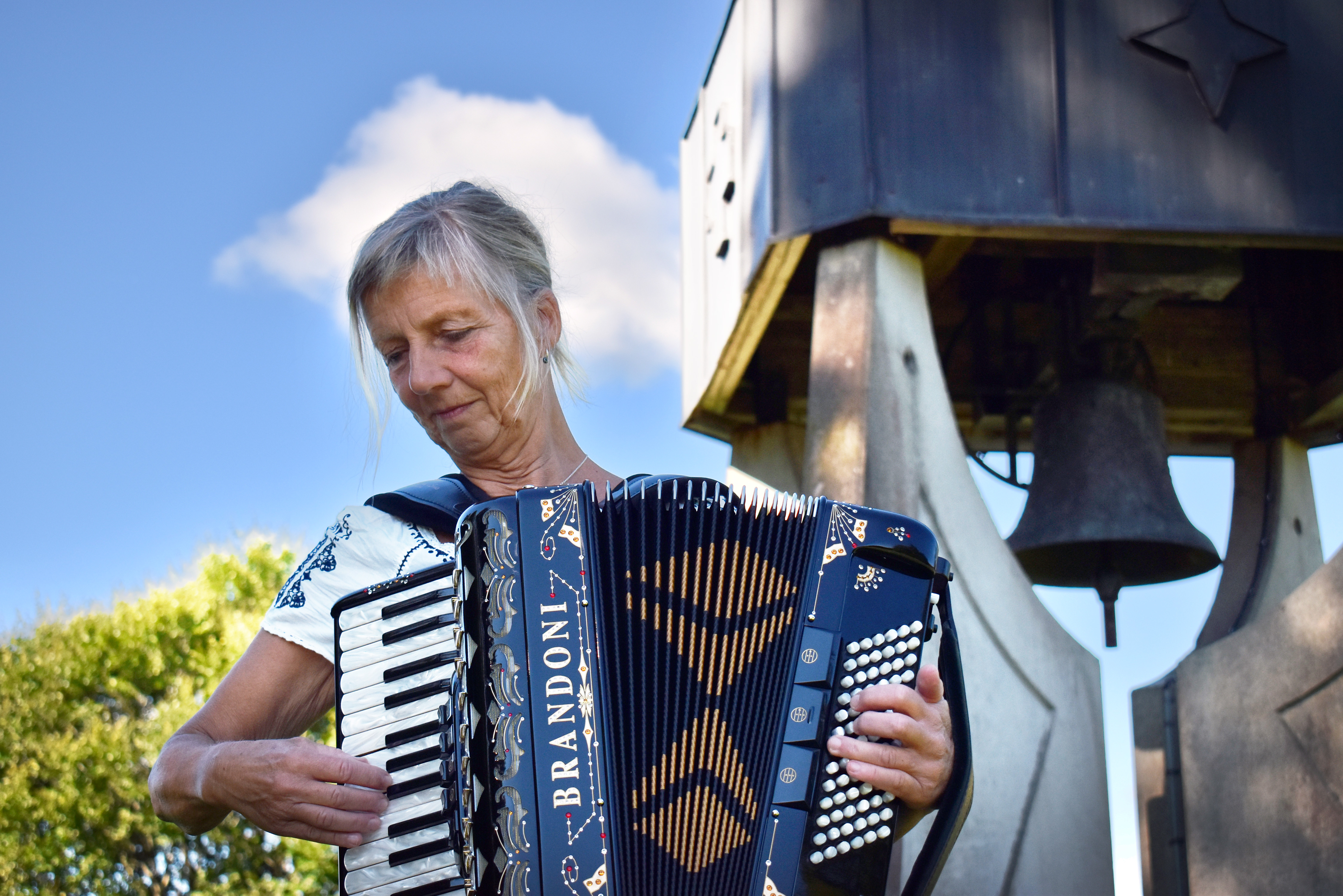 Kvinna spelar dragspel framför klockstapel.