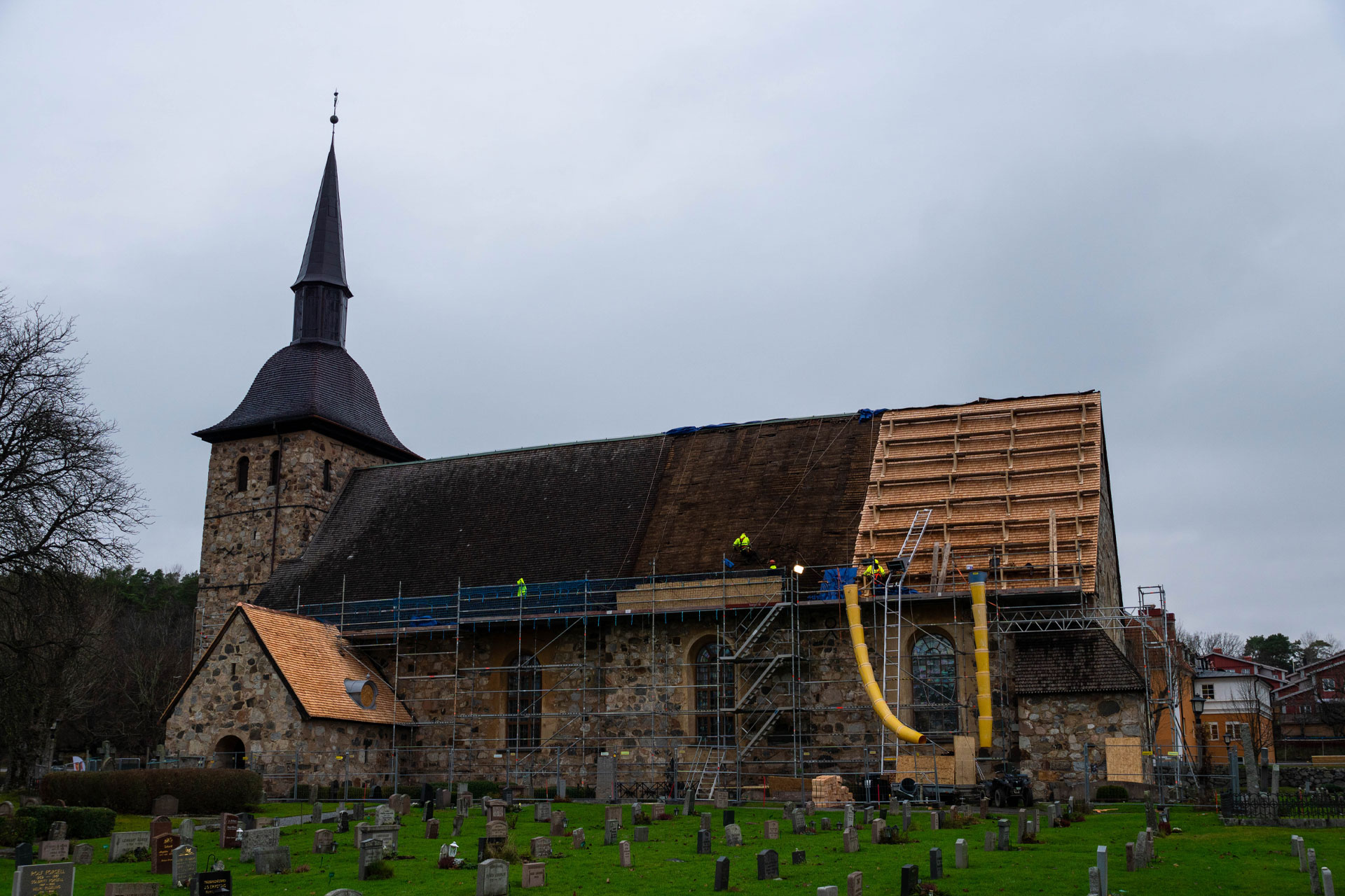 Arbetare tar bort gammal takspån och monterar nytt på Botkyrka kyrkas ena långsida.