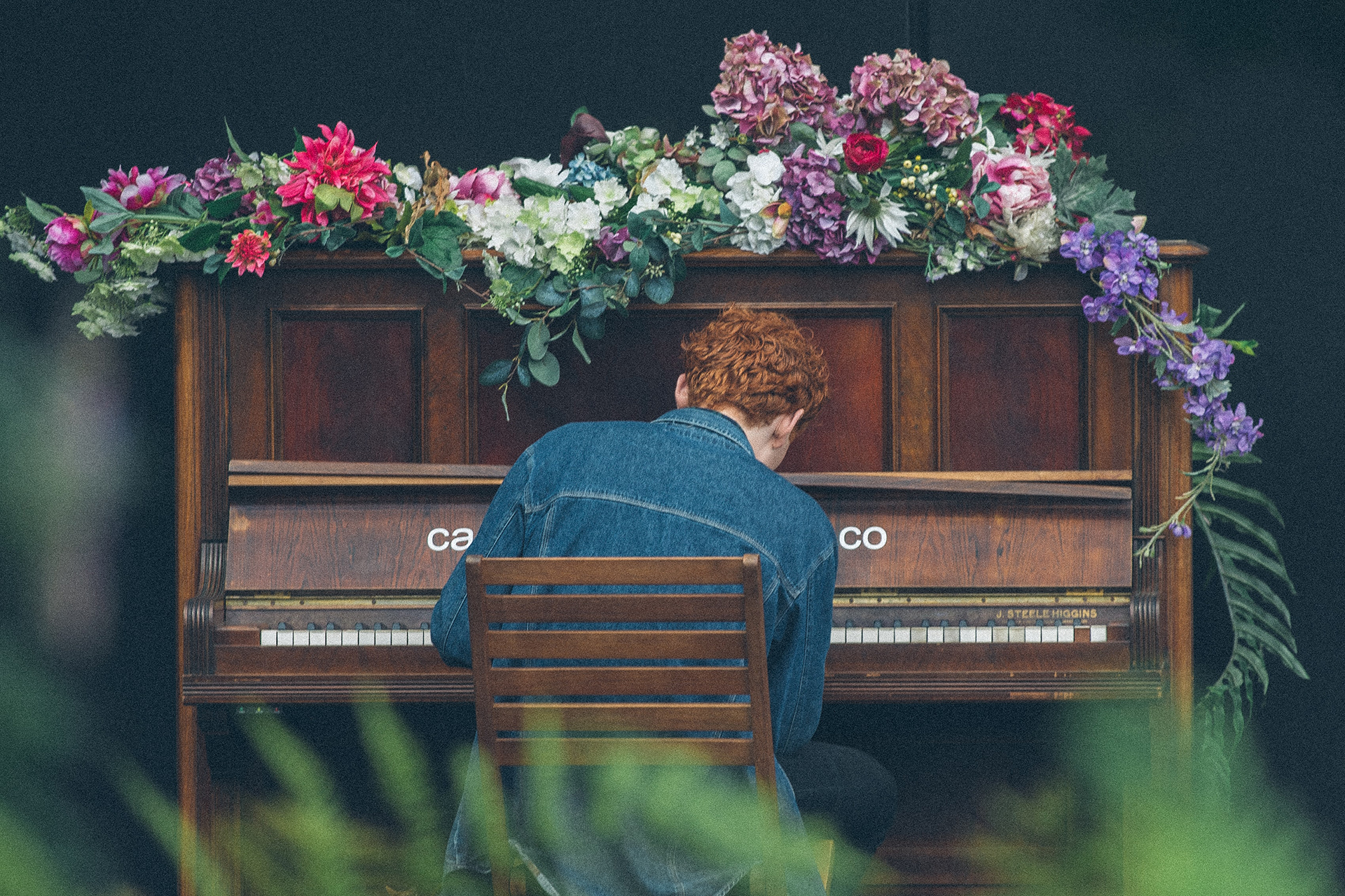 En man som spelar på ett piano överöst av sommarblommor.