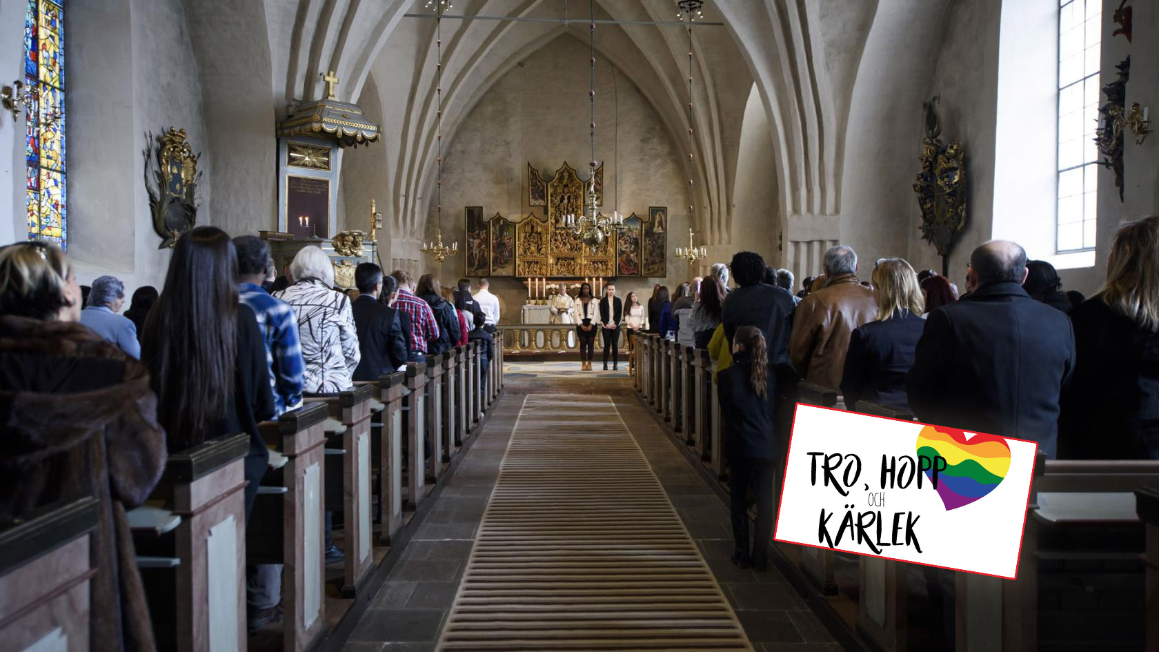 Fullt med människor inne i Botkyrka kyrka, vända bort mot kameran som är riktad mot altaret. I höger hörn står det "Tro, hopp och kärlek", med ett regnbågshjärta