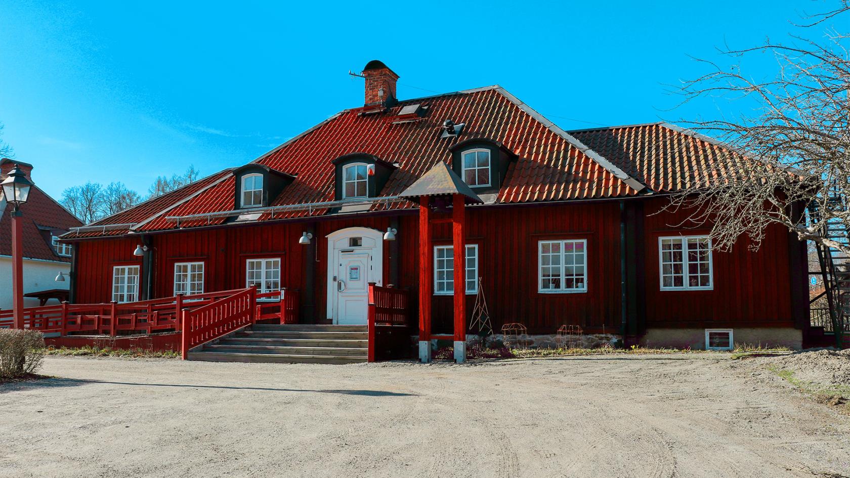 En faluröd träbyggnad med orange tegeltak. I bakgrunden en klarblå himmel. 