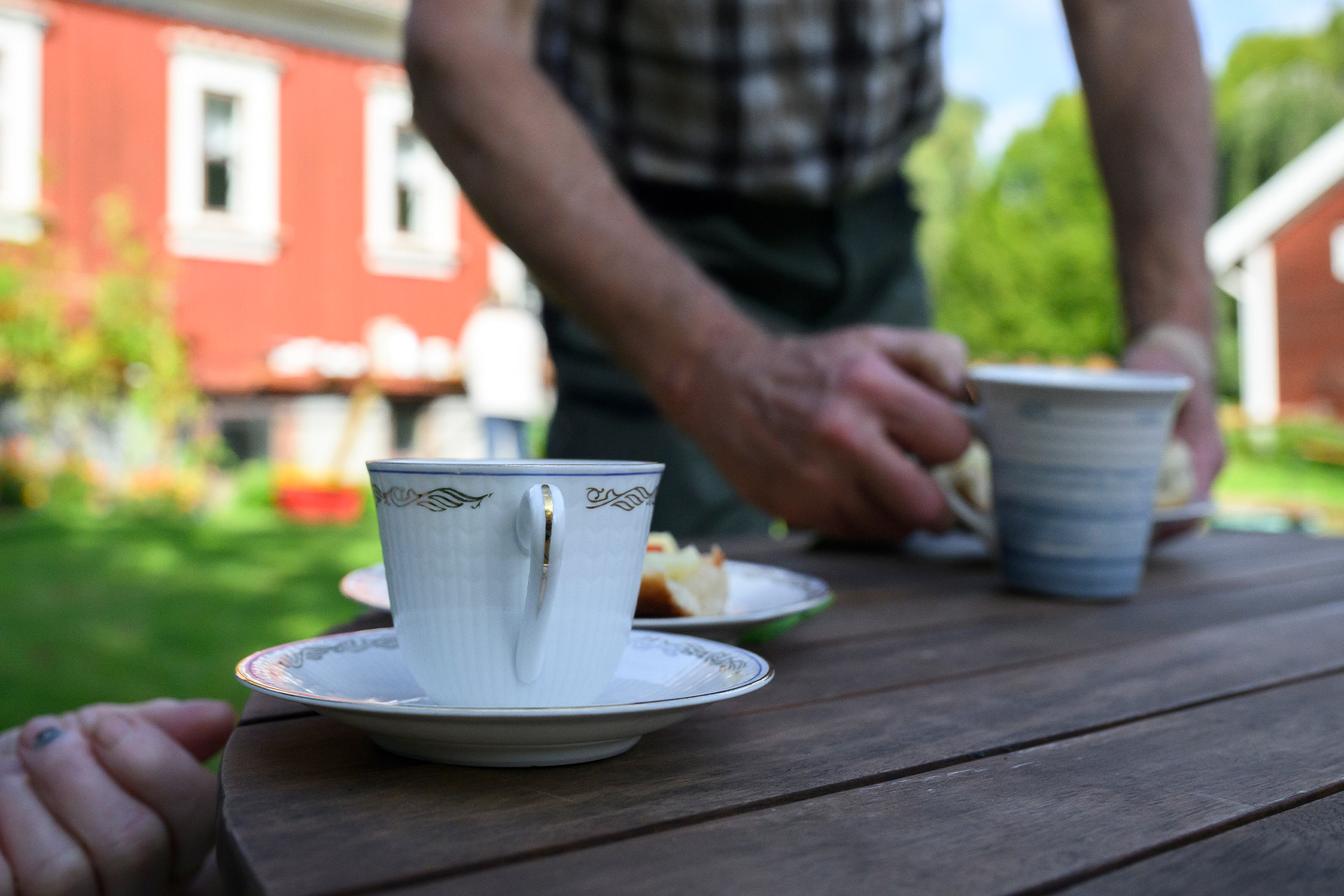 Två personer vid ett bord utomhus på sommaren. På bordet står två kaffekoppar.