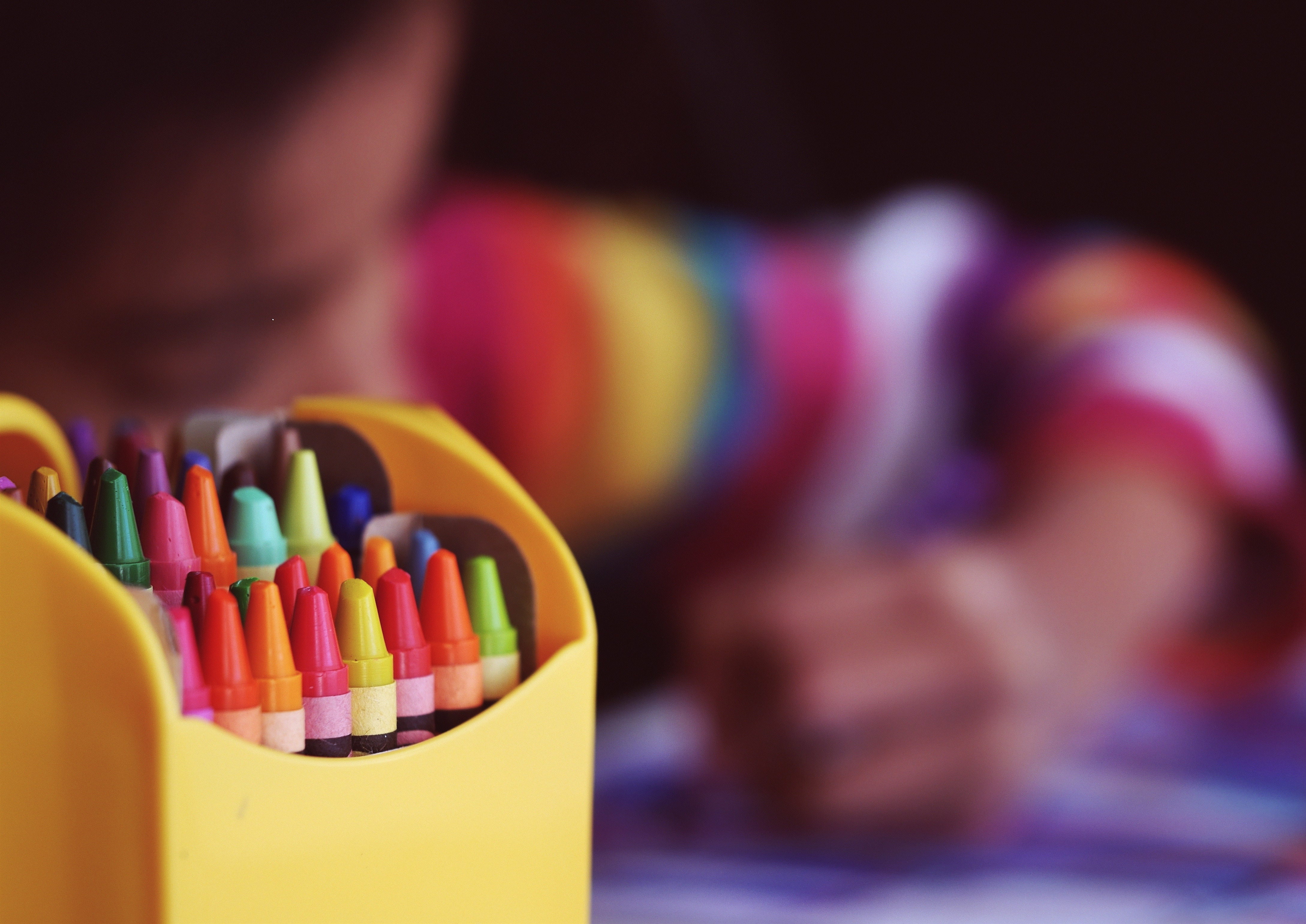 Färgglada målarkritor i en ask. I bakgrunden skymtar ett barn som ritar.