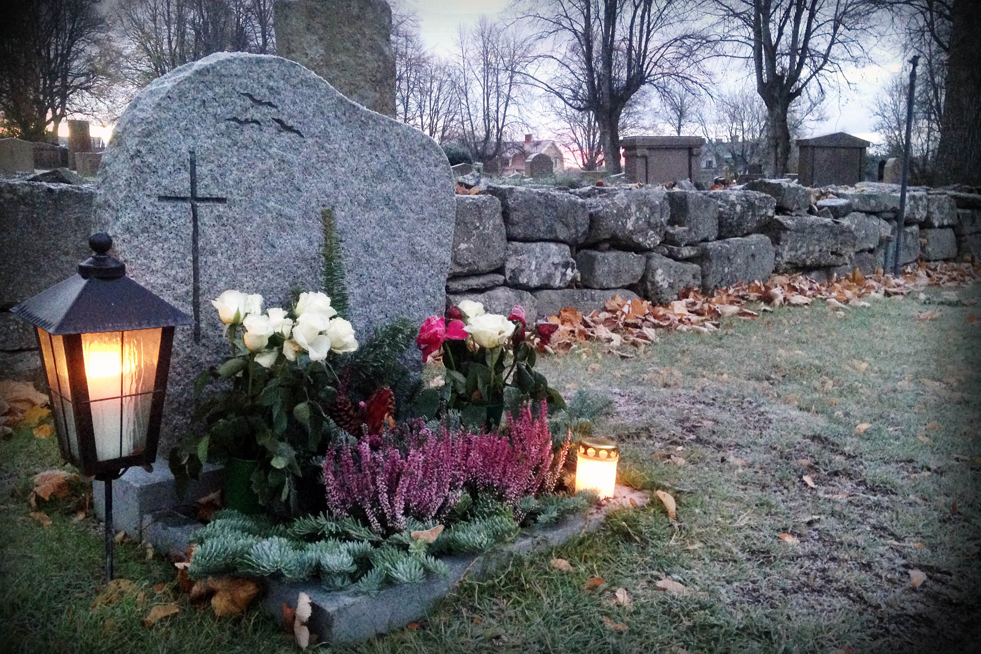 Smyckad grav med blommor och tända lyktor i allhelgonatid.