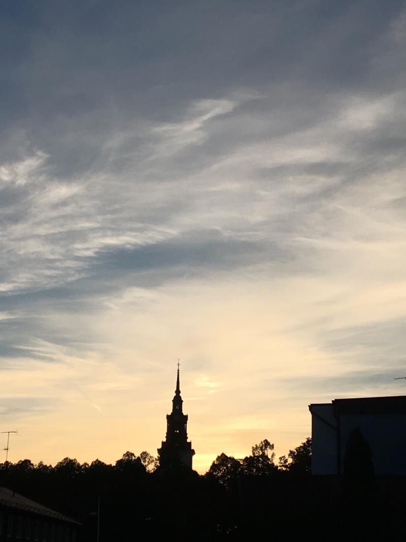 Silhuetten av Västerlövsta kyrka med omgivningar framför en dramatisk kvällshimmel