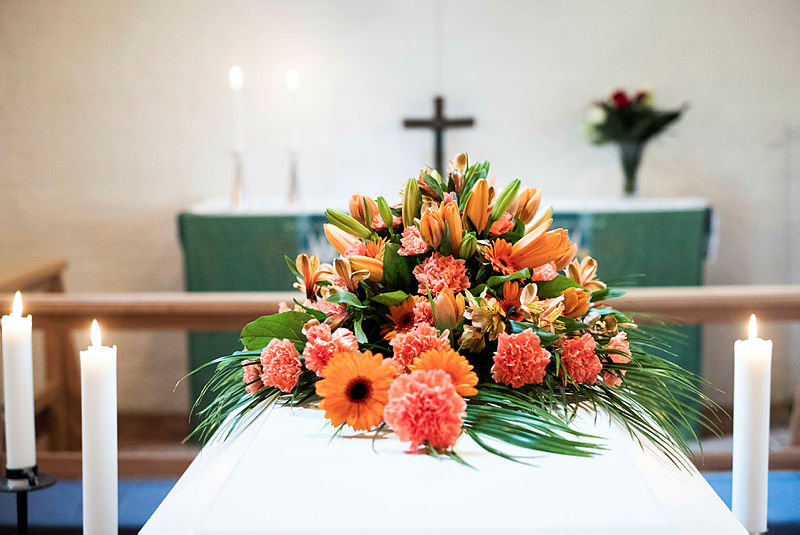 Orangea blommor dekorerade på en kista med vita tända ljus bredvid.