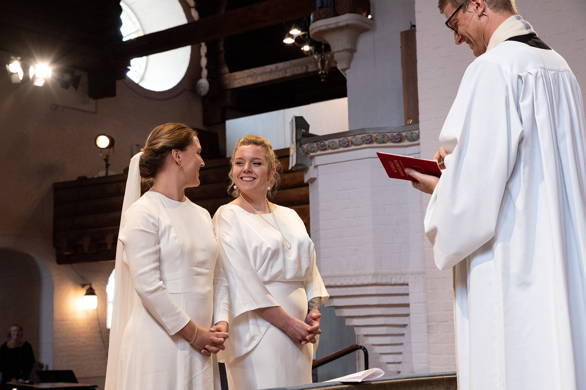 En vigsel mellan två kvinnor i brudklänningar i Masthuggskyrkan. Brudparet står framför prästen.