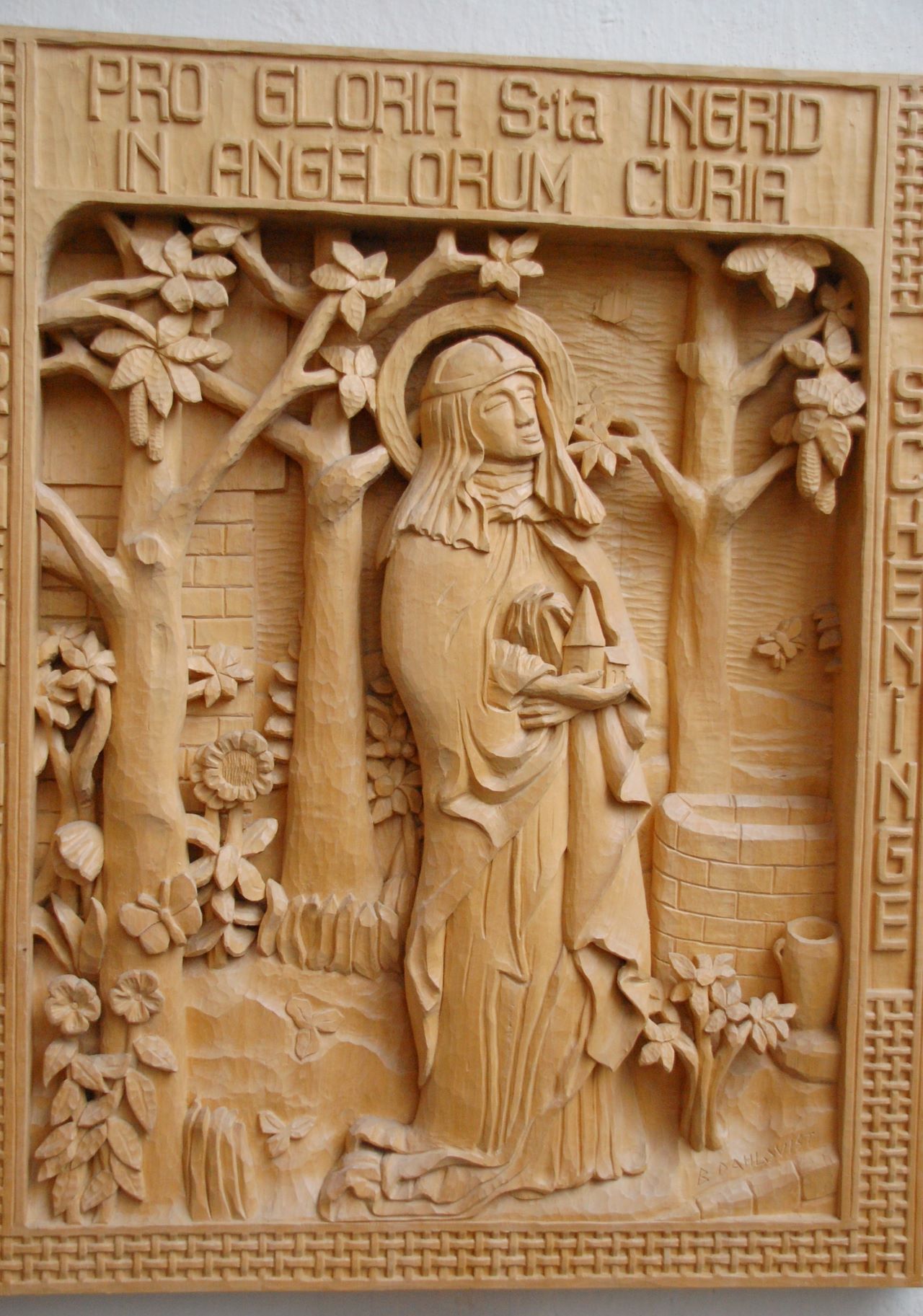 Utskuren relief av S:ta Ingrid. Kvinna med dok på huvudet och håller en kyrka i händerna. Runt omkring finns  utskurna blommor och träd.