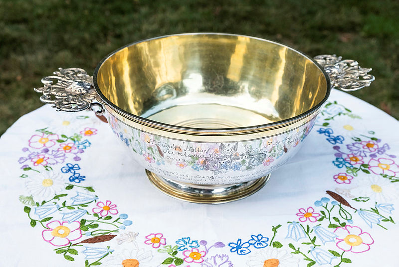 Dopskål i silver på vit broderad duk med blommor.