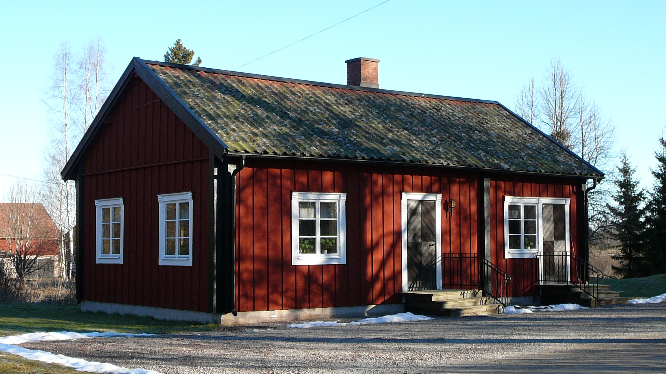 Litet rött hus med svarta knutar och vita fönsterfoder.