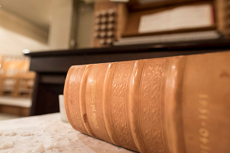 Beige äldre bibel på orgelpall framför kyrkorgel.