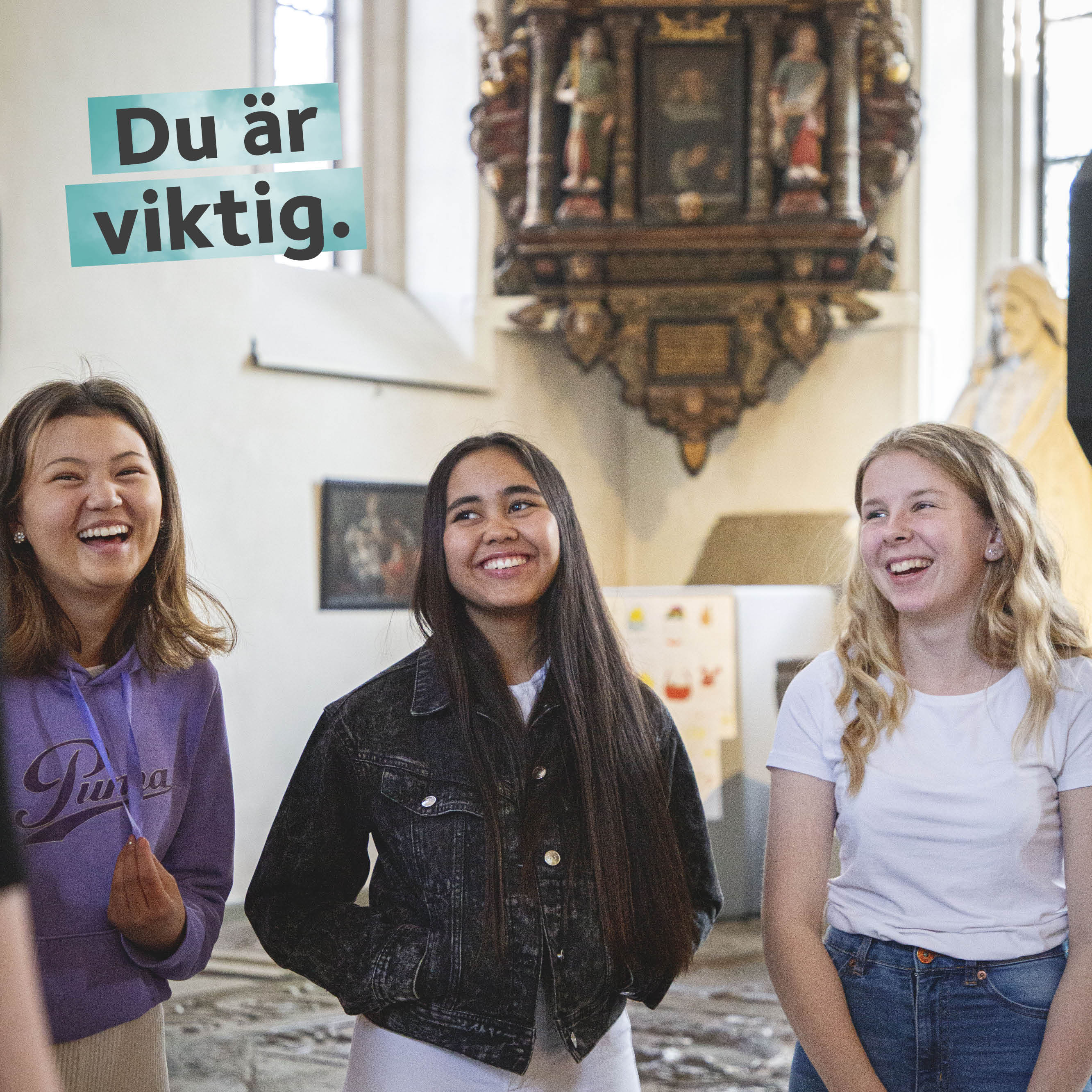 Tre glada unga tjejer står i en kyrka med en altartavla i bakgrunden. En flicka är klädd i lila tröja, en i svart jeansjacka och en i en vit kortärmad tröja.