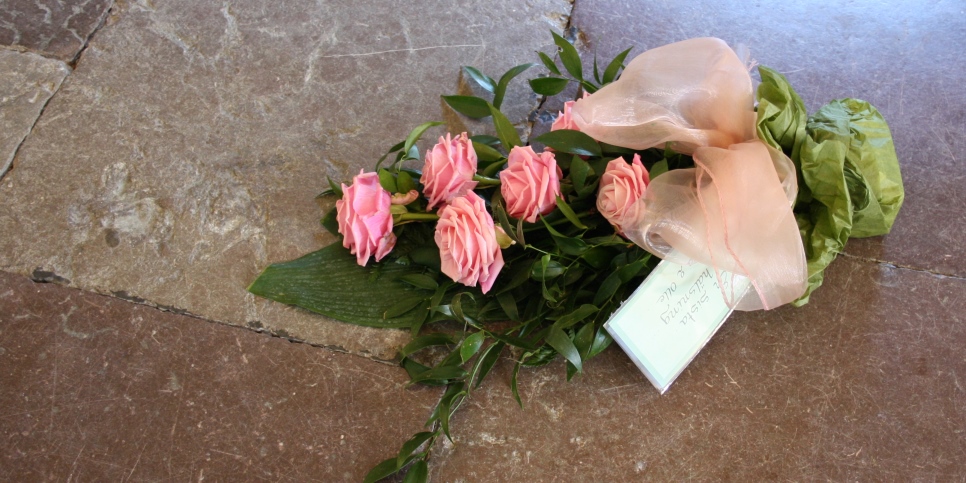 En begravningsbukett rosor ligger på ett kyrkgolv. 
