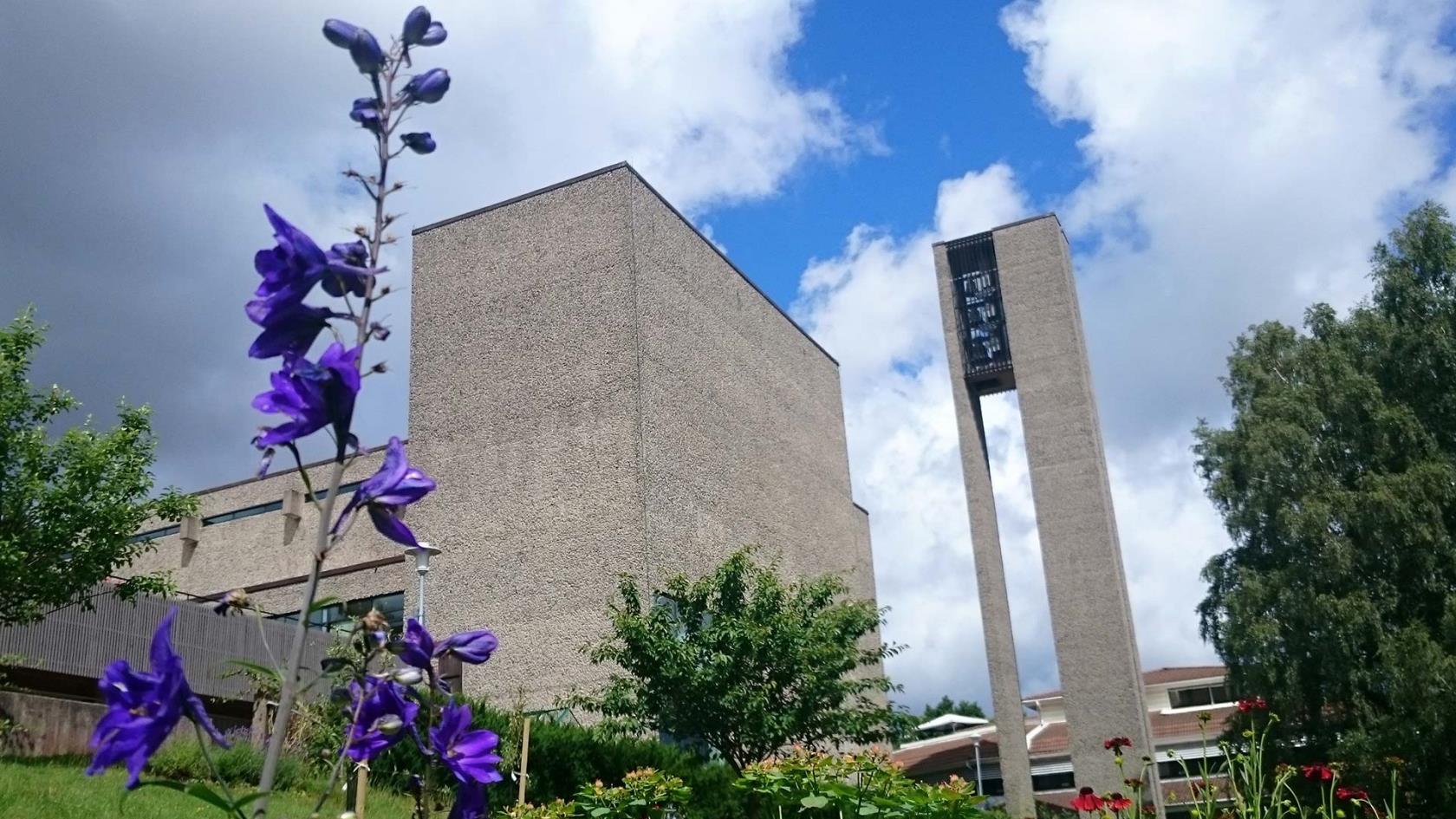 Exteriörbild av Högsbo kyrka. I förgrunden blommar en blå blomma.