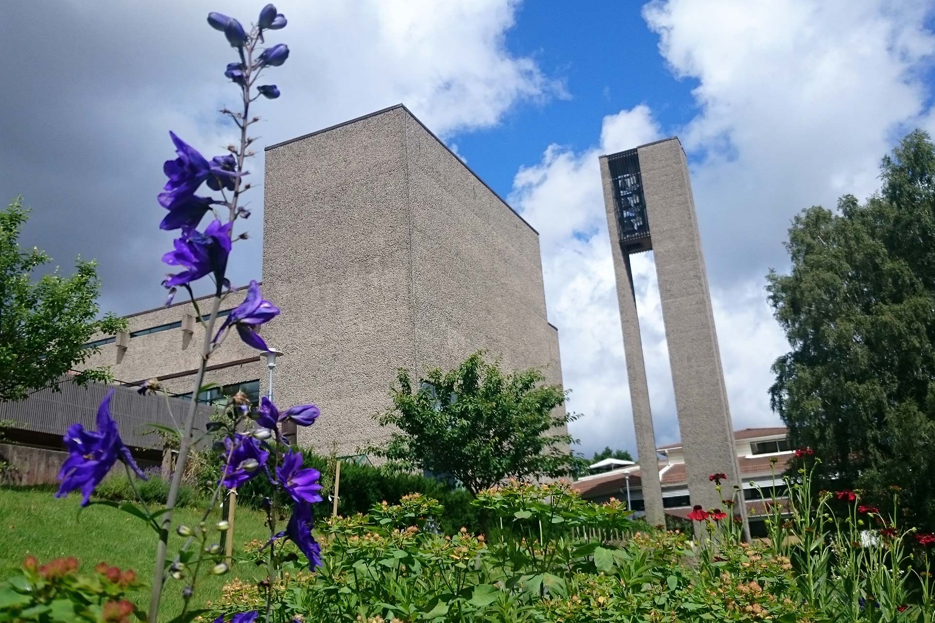 Exteriörbild av Högsbo kyrka. I förgrunden blommar en blå blomma.