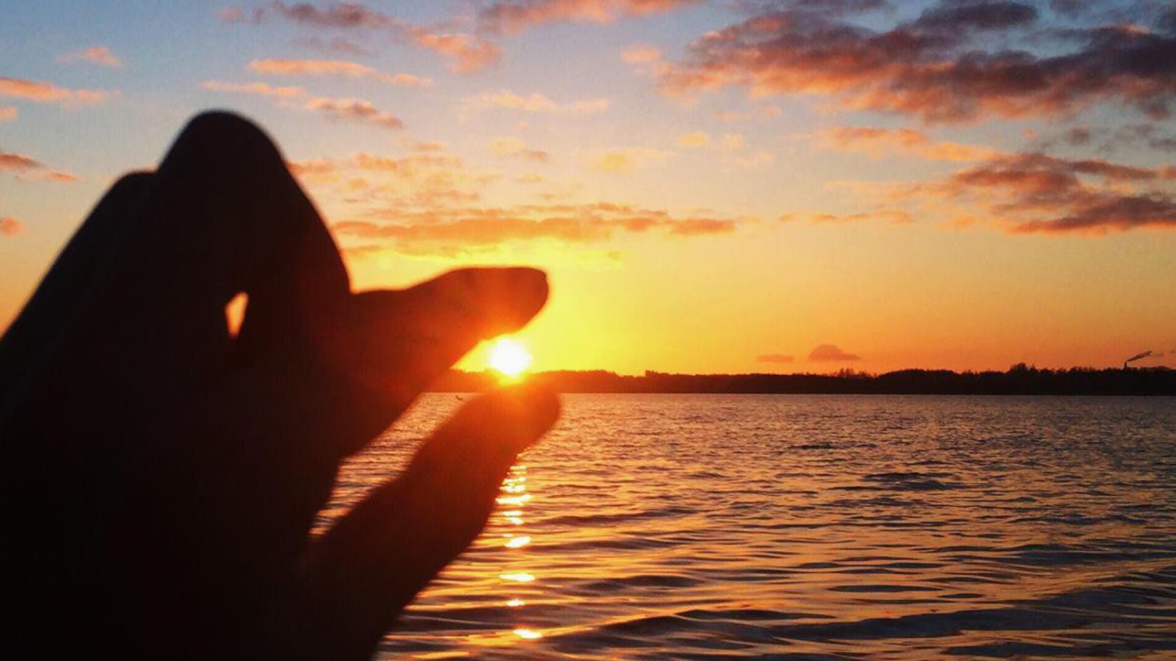 Solnedgång och en hand som håller fingrarna så det ser ut som att den håller i solen