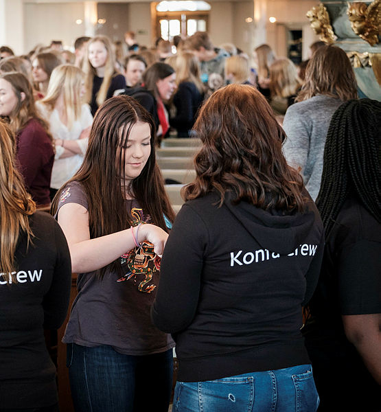 Unga tjejer i kyrkan i bakgrunden och konfacrew i svarta tröjor i förgrunden.