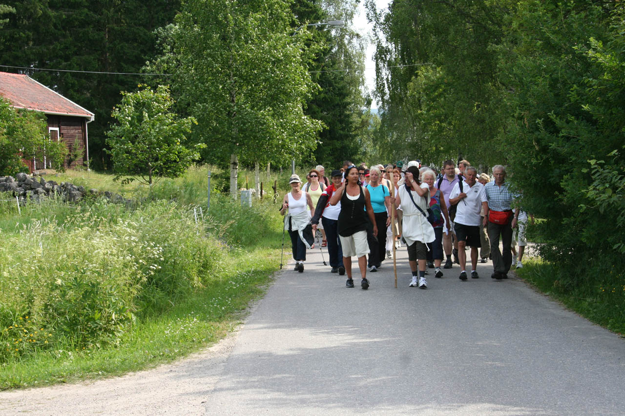 Pilgrimsvandrare längs en väg omgiven av sommargrönska