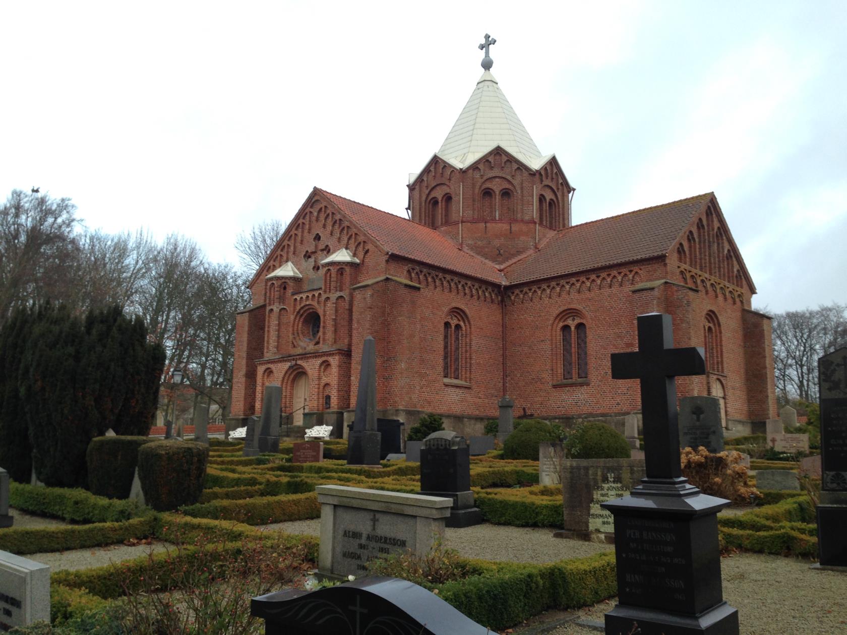 Korskyrka i röd tegel med torn i mitten av kyrkan.