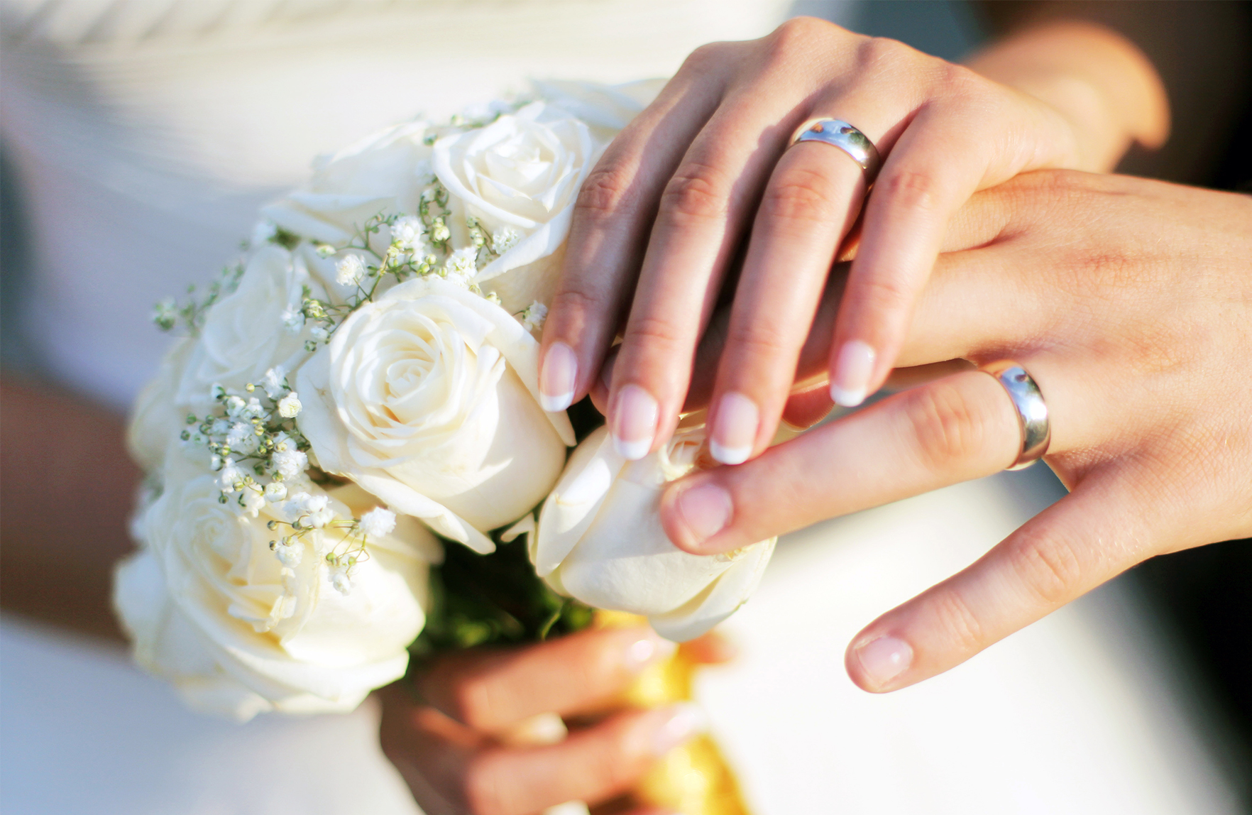 Två händer med ringar på två fingrar ligger ovanpå en bukett med vita rosor.