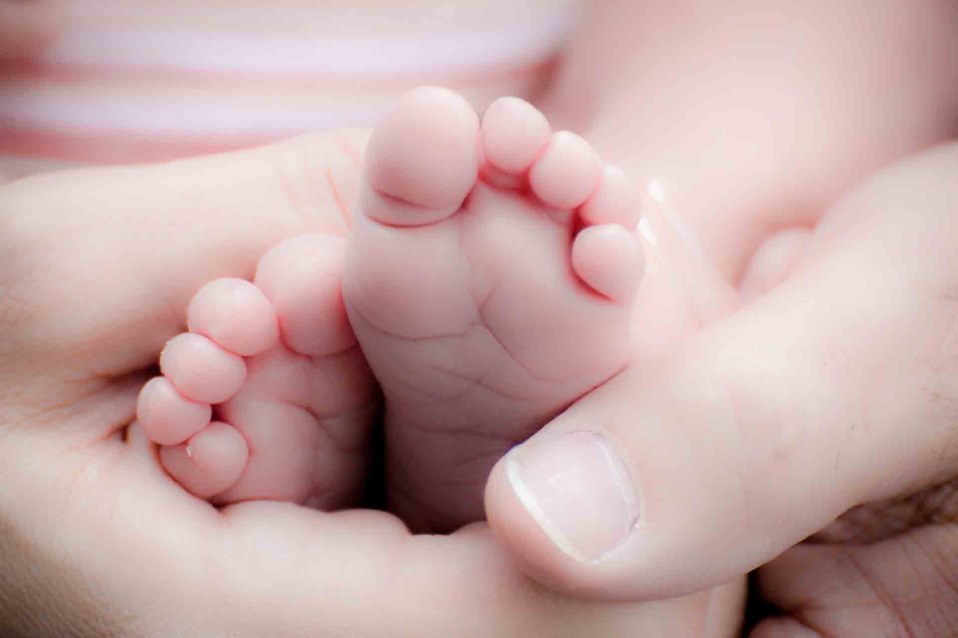 Nakna små babyfötter som hålls om av vuxens händer.