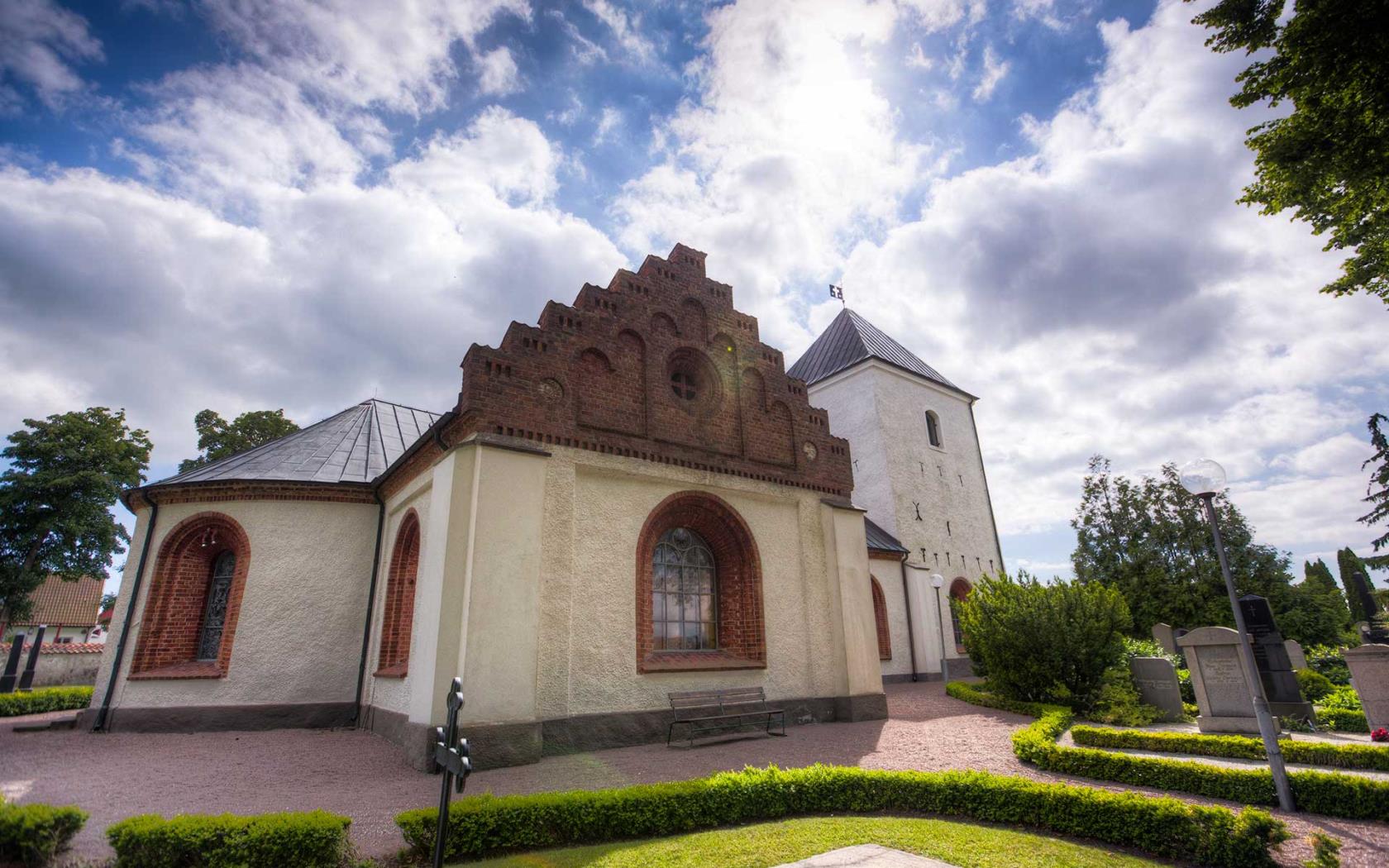 Vitputsad landsortskyrka med röda tegeldetaljer.