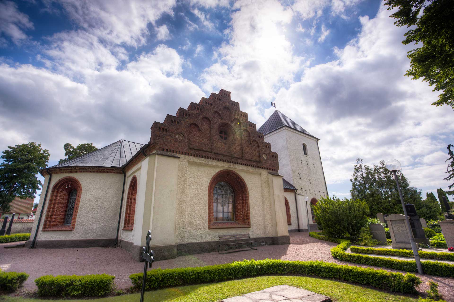 Vitputsad landsortskyrka med röda tegeldetaljer.