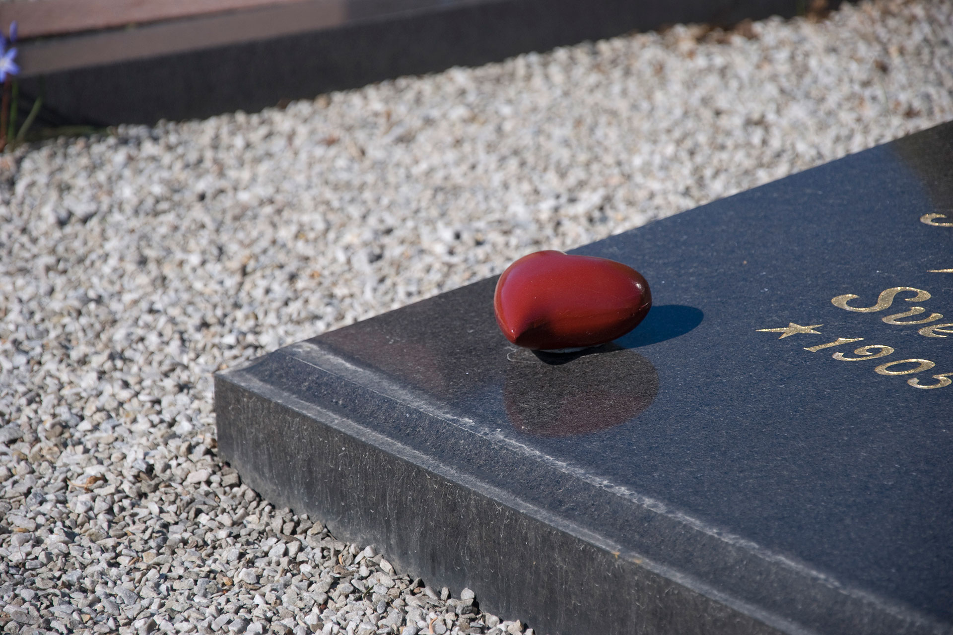 Liggande svart gravsten med ett rött keramikhjärta.
