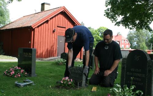 Två kyrkogårdsarbetare riktar en gravsten.