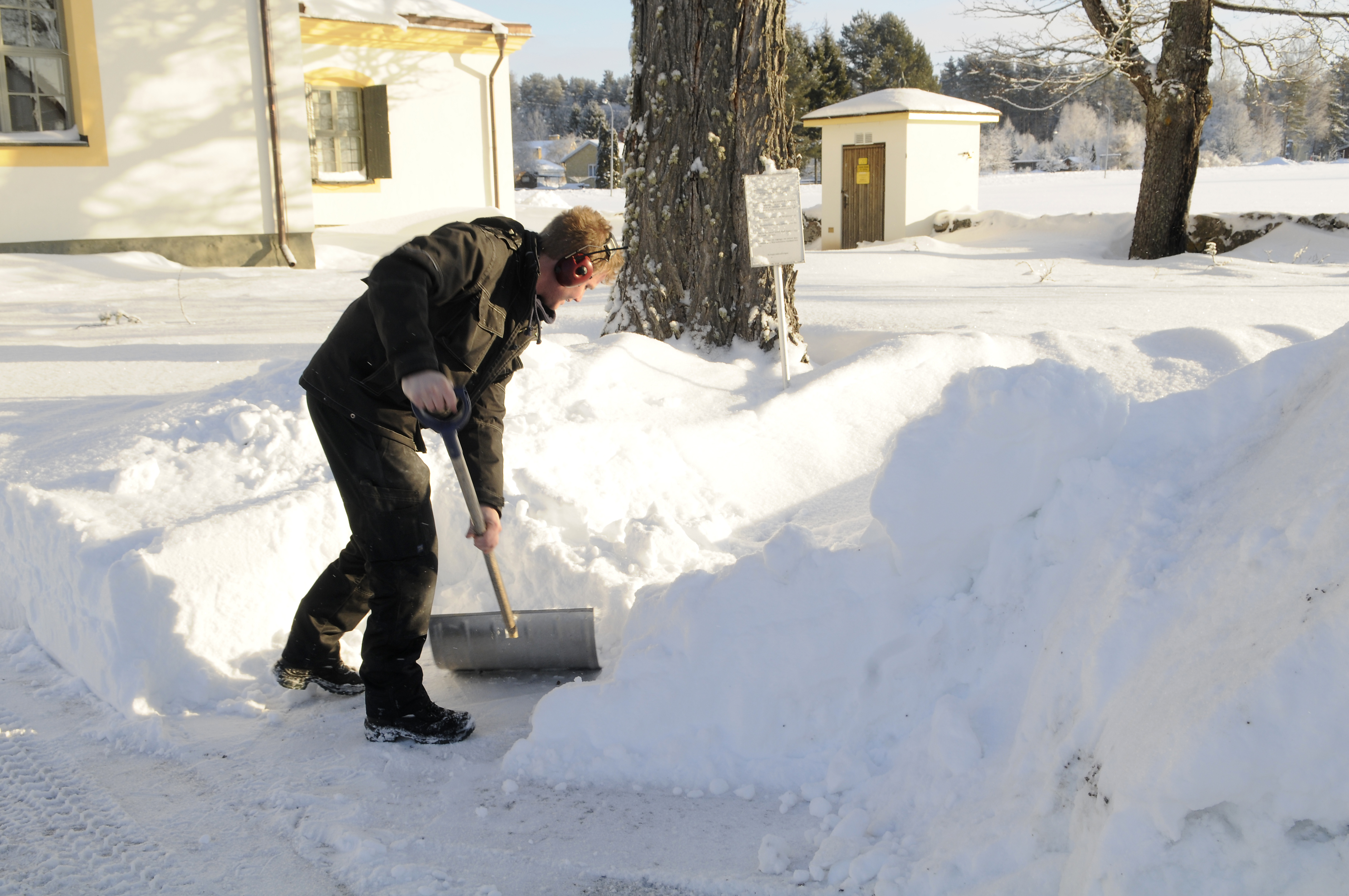 En vaktmästare skottar snö framför kyrkobyggnad.