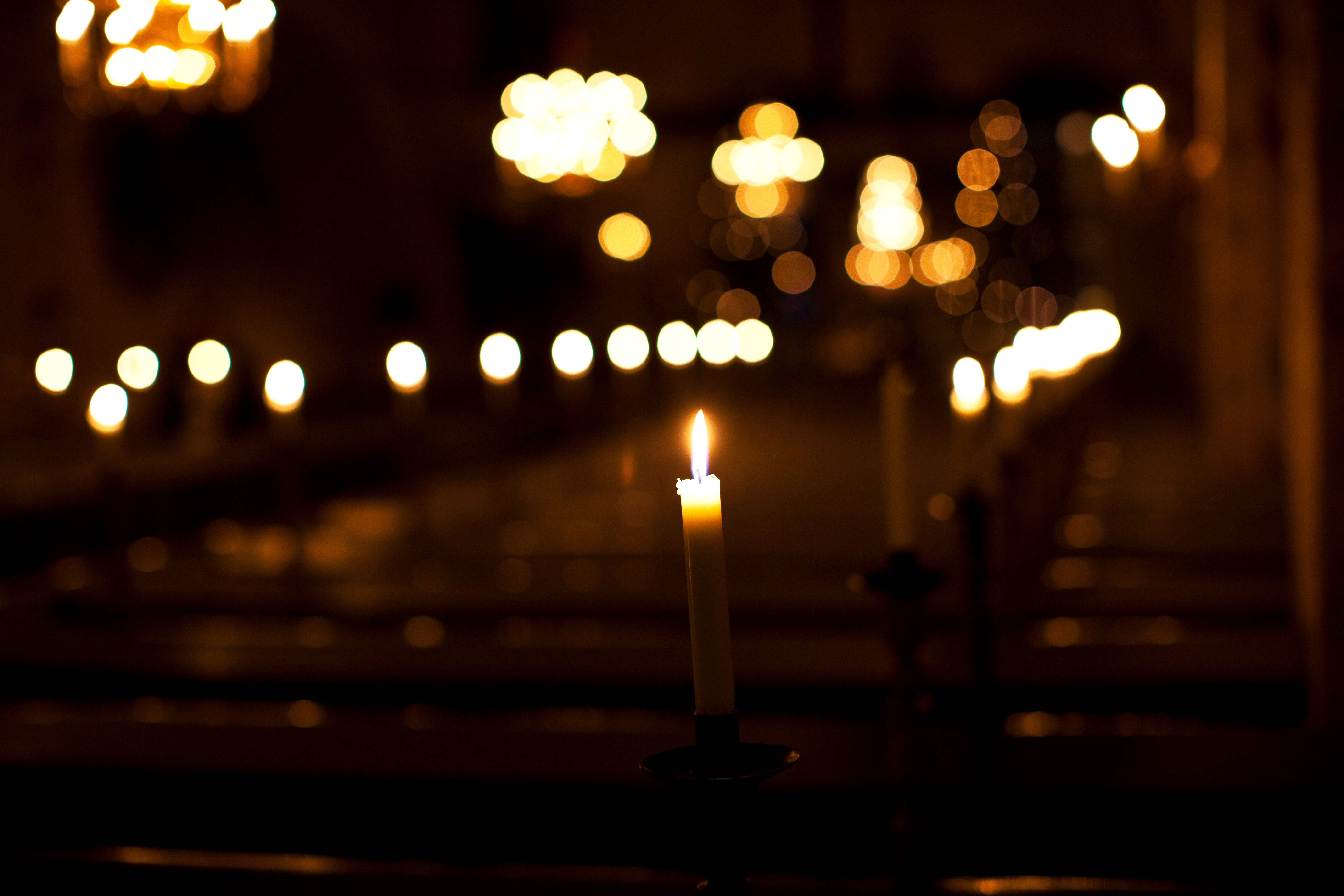 Suddig bild av tända ljus som lyser i en mörk kyrka.