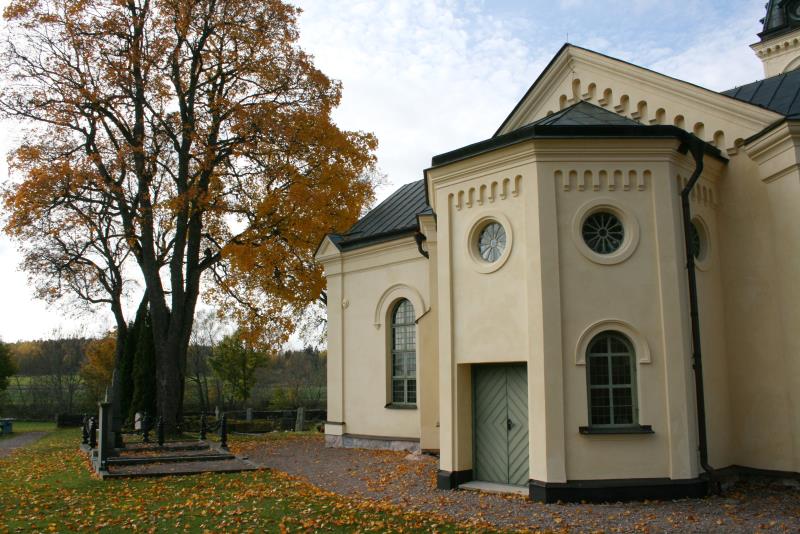 Några träd med brandgula löv står vid en gulvitputsad kyrka.