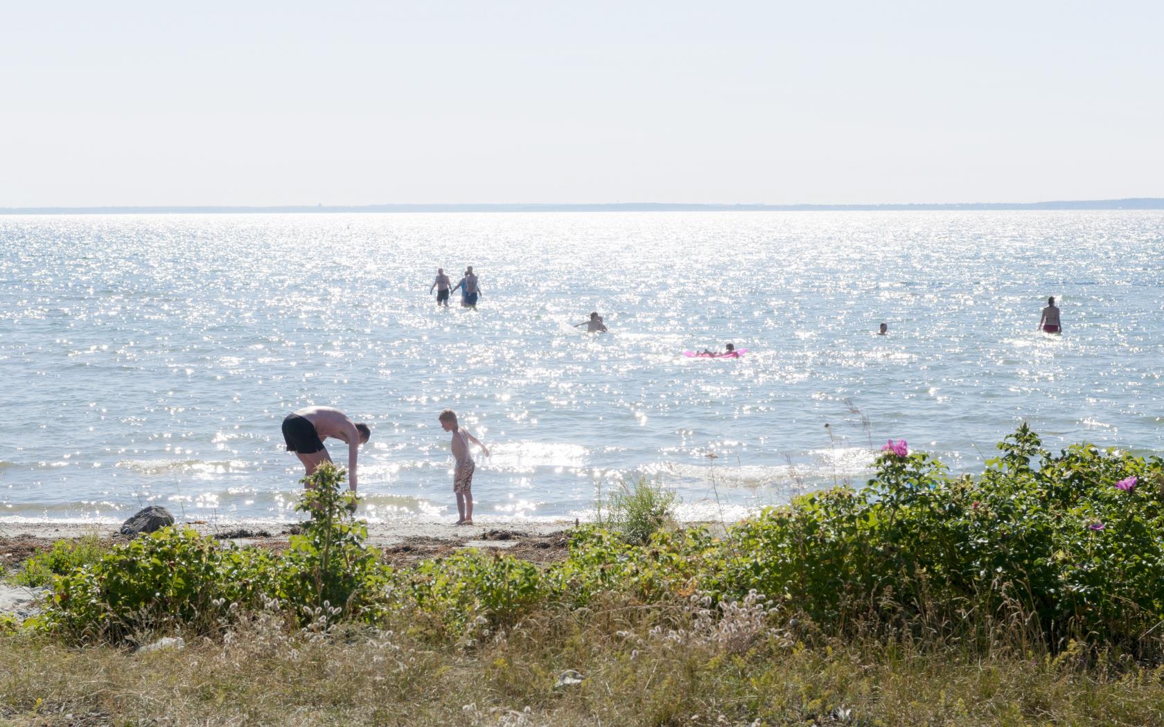 Människor som badar i långgrunt vatten på en strand.