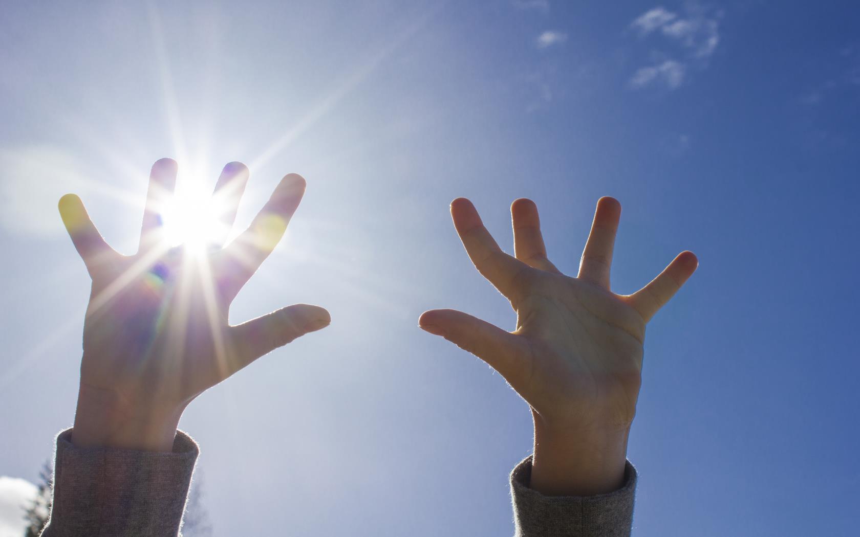 Ett barn sträcker upp händerna mot himlen. Solen lyser igenom fingrarna.