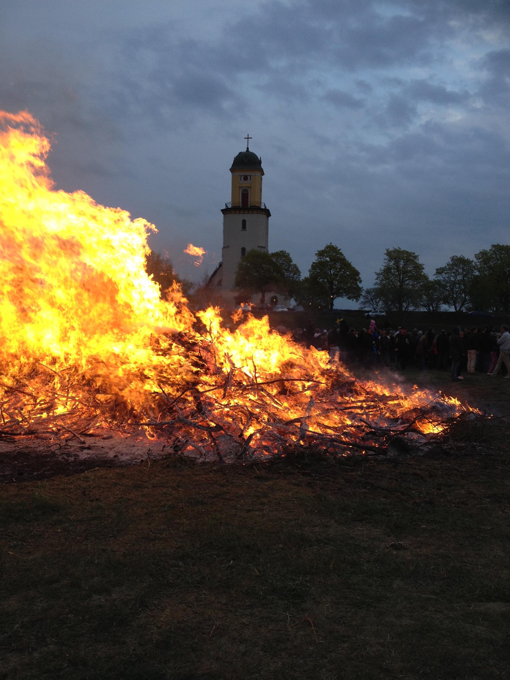 En stor majbrasa och en kyrka i bakgrunden.