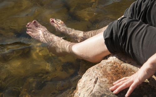 Någon sitter på en sten och doppar fötterna i vattnet.