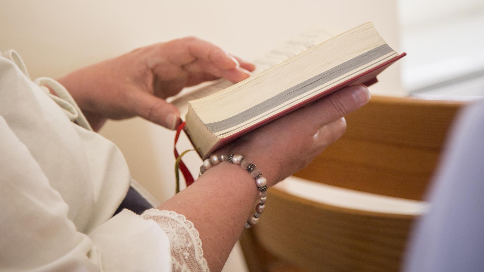 En person sitter och bläddrar i en psalmbok.