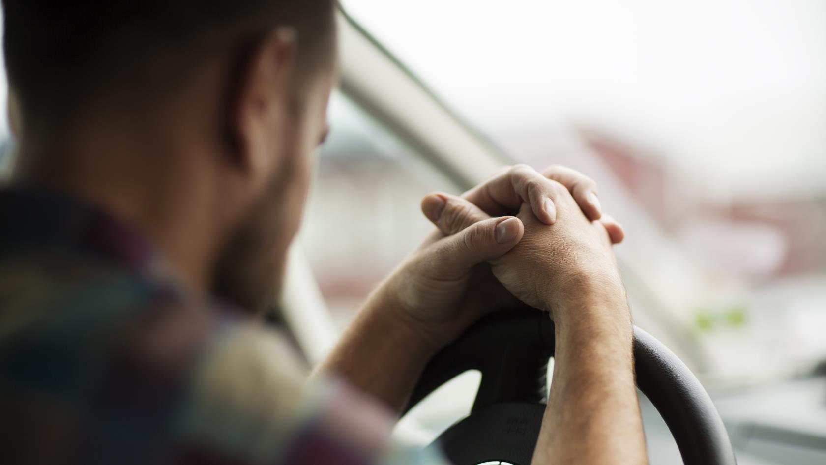 En man sitter i bilen med händerna knäppta på ratten.