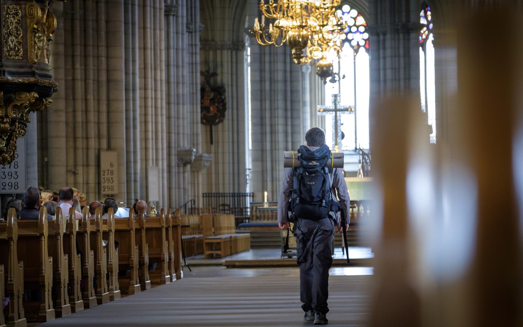 En man med stor ryggsäck går mellan kyrkbänkarna i Uppsala domkyrka.