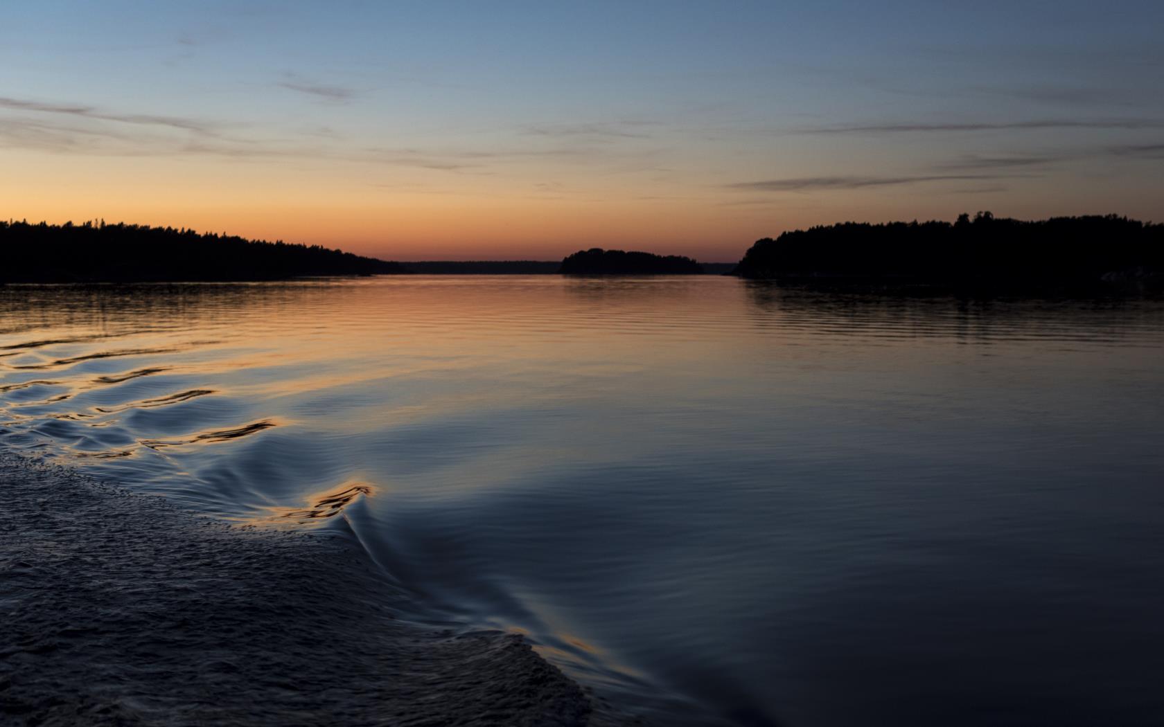 Vågor från en båt i stilla vatten vid solnedgången.