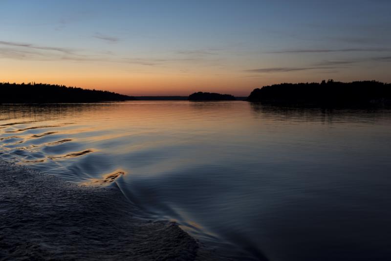 Vågor från en båt i stilla vatten vid solnedgången.