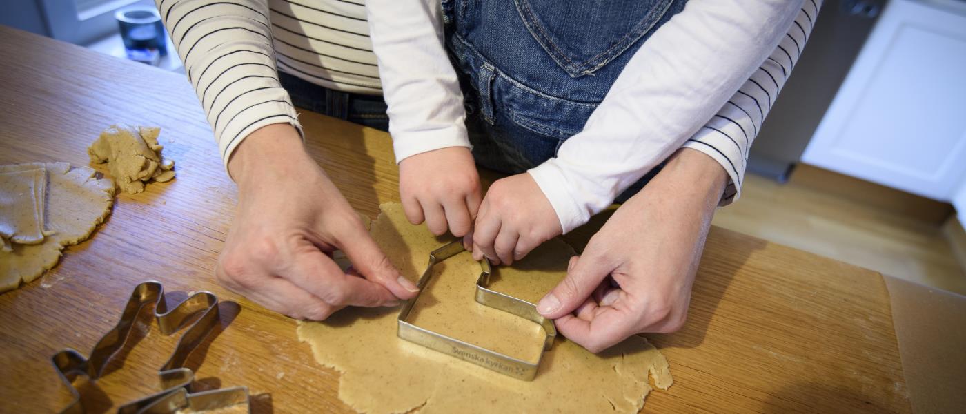 En vuxen hjälper ett barn trycka ner en form i pepparkaksdegen på bordet.