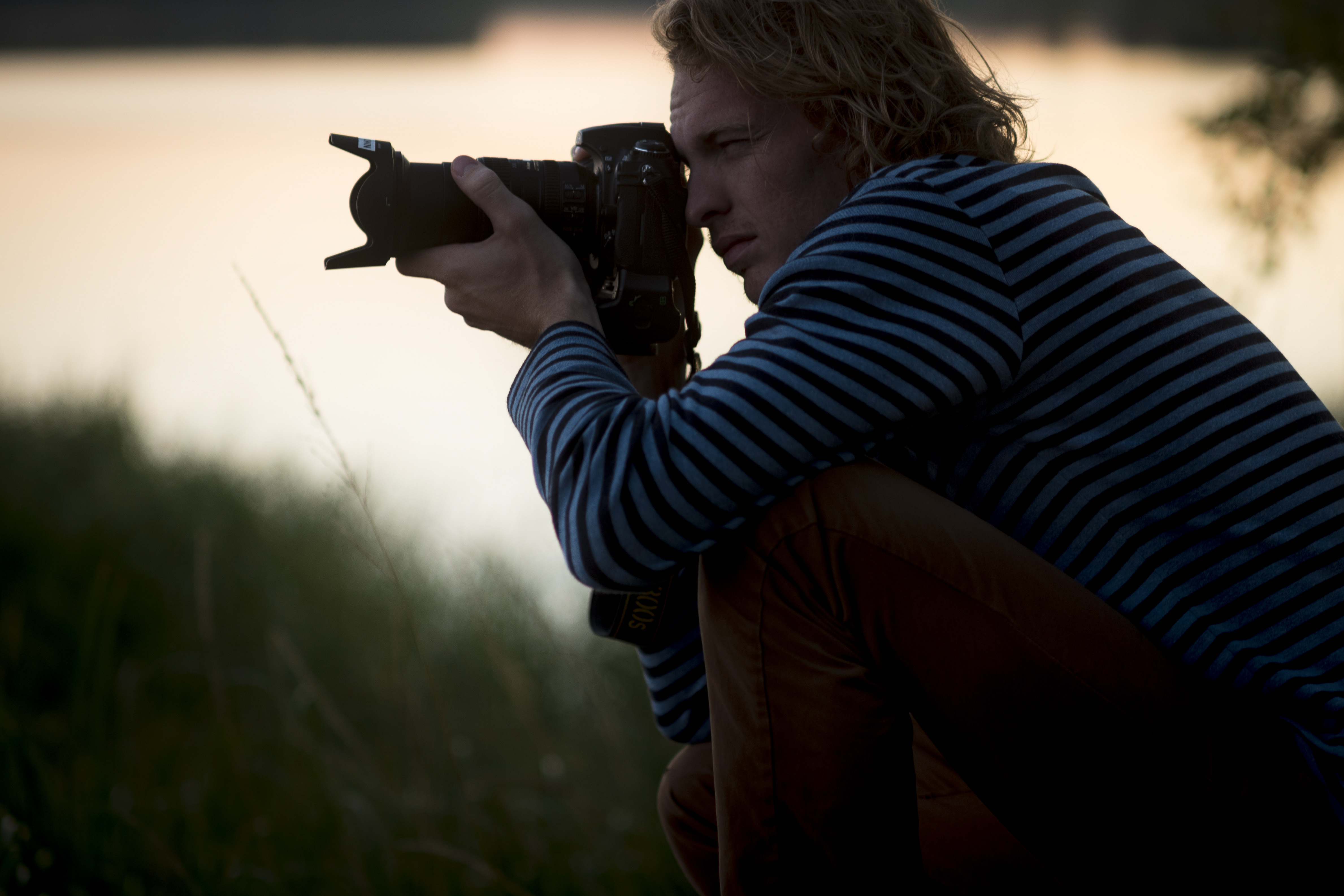 En man sitter ute i naturen och fotograferar.