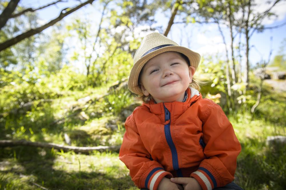 En liten pojke med halmhatt sitter ute i naturen och ler mot kameran.