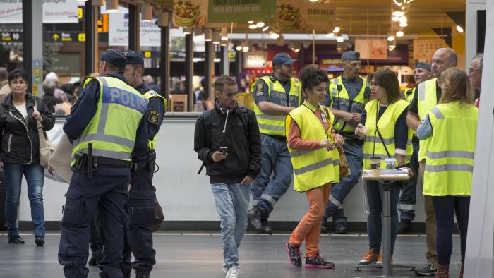 Några ordningsvakter, två poliser och några personer i gula reflexvästar står inne på en galleria.