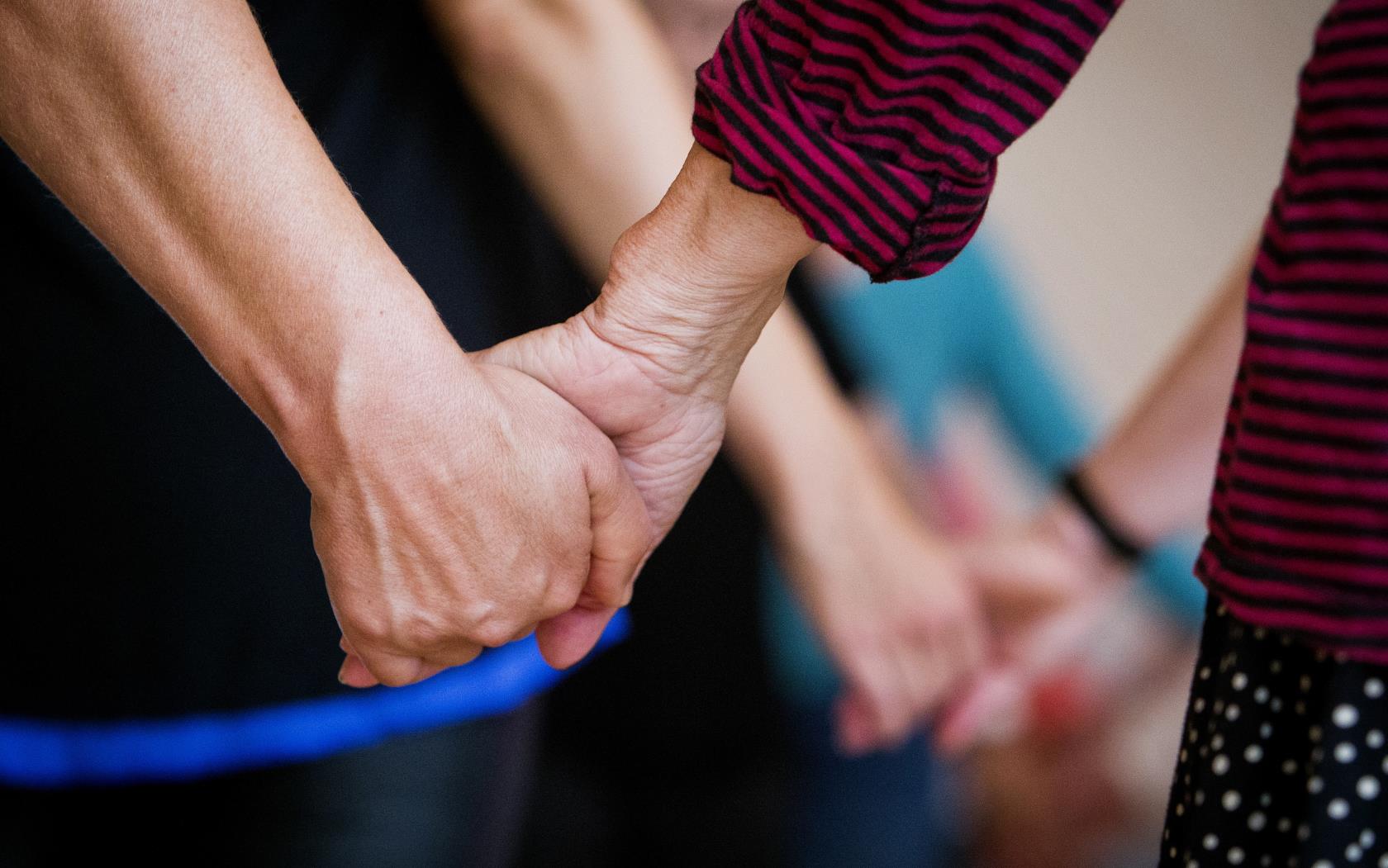 Närbild på två personer som håller hand. I bakgrunden håller fler par varandra i hand.