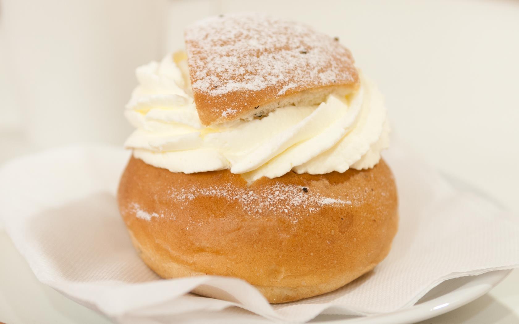 En semla och en kaffekopp står serverat på ett bord.