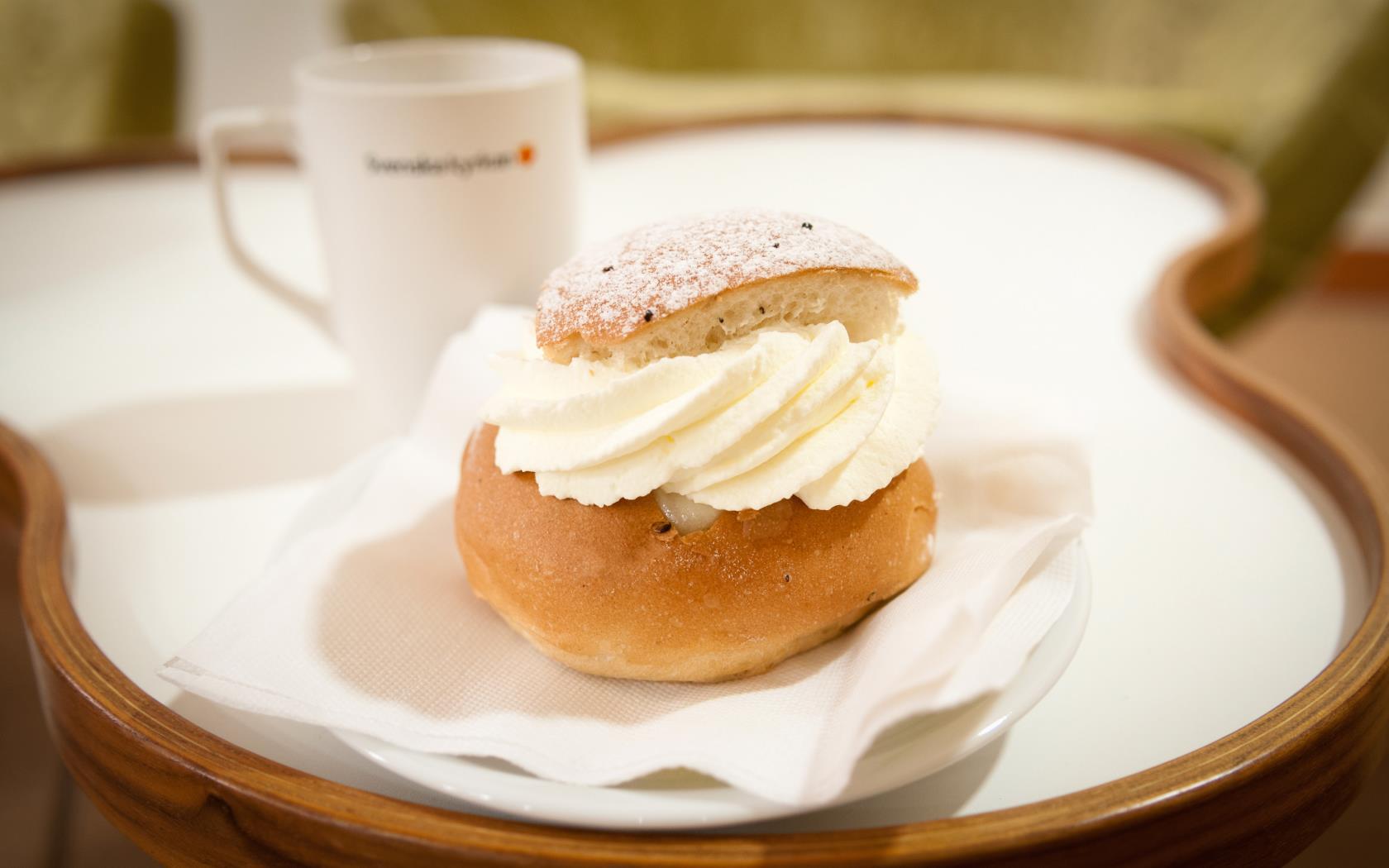 En semla och en kaffekopp står serverat på ett bord.