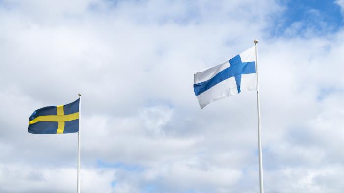 Två flaggstänger med finska och svenska flaggan mot en blå och molnig himmel.